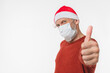 © InsideCreativeHouse - Caucasian man in red Santa Claus hat wearing protective face mask against coronavirus Covid 19 showing thumb up isolated in white background. Pandemic Christmas New Year concept
