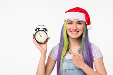 Happy young caucasian girl woman in red Santa Claus hat pointing at clock for celebration New Year`s Eve Christmas isolated in white background. Winter holidays concept