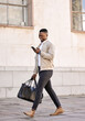 © peopleimages.com - Business, black man and smile with phone for commute schedule, urban travel and communication. Male person, mobile and walking with luggage for appointment, morning journey and interview opportunity