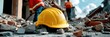 © Inlovehem - Yellow hard hat on construction site debris, blurred workers in background.