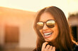 © peopleimages.com - Face, smile and sunglasses with woman outdoor in summer for holiday, travel and sunset. Laughing, shades and wellness with happy tourist person in urban neighborhood for break or trip abroad