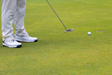 a white golf ball on a tee and a green field ready to be hit with a wood golf stick as a start to a game of golf.