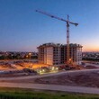 © LIGHTFIELD STUDIOS - A photo of a construction site at dusk with bright construction lights illuminating the area, showcasing the transition from day to night in a bustling real estate development zone