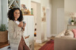 © mavoimages - Smiling young African woman drinking coffee in her kitchen at home
