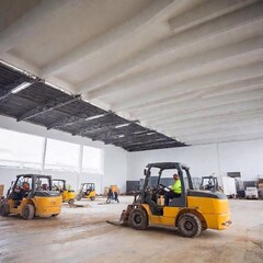 A photo of construction activity inside a warehouse being built, featuring workers operating forklifts to move materials, and construction tools and equipment set up around the site