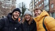 © Pinklife - A group of three friends, two men and a woman, share a moment of laughter on a city street, dressed warmly for the cold weather in a vibrant city setting.
