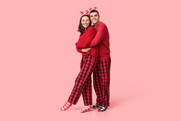 Wall Mural - Happy young couple in Christmas pajamas hugging on pink background