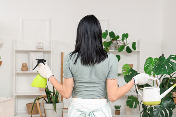 Wall Mural - Young woman with watering can and sprayer at home, back view