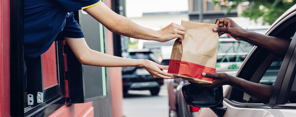 Hand Man in car receiving coffee in drive thru fast food restaurant. Staff serving takeaway order for driver in delivery window. Drive through and takeaway for buy fast food for protect covid19.