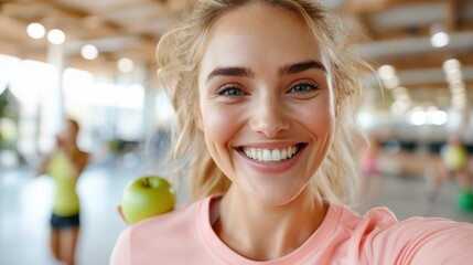 A young, energetic woman taking a selfie in the gym while holding a green apple, showcasing her vibrant lifestyle, fitness, and love for healthy living.