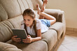 © N Hiraman/peopleimages.com - Weekend, sofa and child with tablet in home for online learning, watching movies and internet videos. Relax, living room and young girl on digital tech for games, streaming cartoons and website