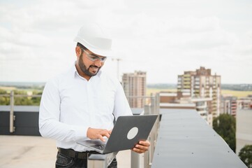 Indian male engineer wearing helmet at construction site. Copy space. Real estate