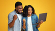 © Prostock-studio - Smiling African American Couple Watching Sports On Laptop Together And Cheering, Standing Over Yellow Background With Copy Space