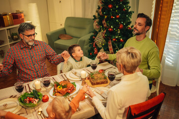 Wall Mural - Family holding hands and praying before christmas dinner