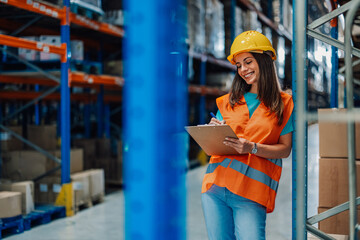 Wall Mural - Female warehouse worker checking inventory using clipboard