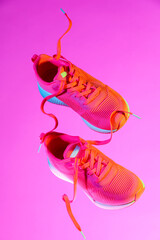 Canvas Print - Pair of stylish sneakers in air against pink background in neon lights