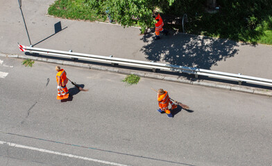 Municipal cleaners manually sweep the city roadway