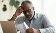 © blinkstud.io - Older man with serious expression reading document sitting at desk with laptop, dealing with important paperwork, managing finances or health-related issues, learn written information looks concerned