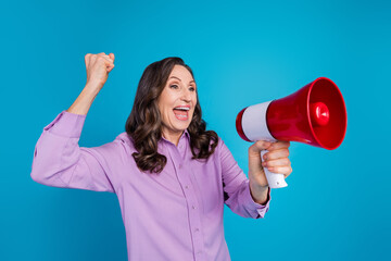 Photo of adorable lucky woman wear violet shirt rising fist yelling loud speaker empty space isolated blue color background