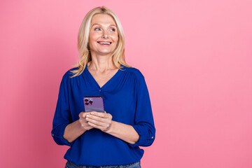 Photo portrait of pretty senior female hold gadget look empty space wear trendy blue outfit isolated on pink color background