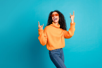 Wall Mural - Photo of shiny attractive young lady dressed knitted pullover showing hard rock signs empty space isolated blue color background