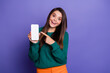 © deagreez - Portrait of pretty young girl point finger empty space phone screen wear sweater isolated on violet color background