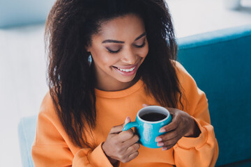 Photo of attractive young woman sit couch holf coffee cup dressed orange outfit cozy day light home interior living room