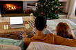 © Wavebreak Media - multiracial couple relaxing by fireplace, watching laptop near Christmas tree at home, copy space