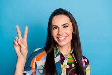 Wall Mural - Photo portrait of attractive young woman smile show v-sign dressed stylish colorful print clothes isolated on blue color background