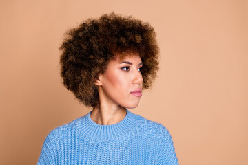 Wall Mural - Photo of young funky american lady with brown hair chevelure in blue knitted sweater looking empty space isolated on beige color background