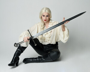 Sticker - Full length portrait of female model wearing vintage gothic fantasy blouse, leather pants and white blonde hair, kneeling holding sword weapon, isolated figure on studio background.