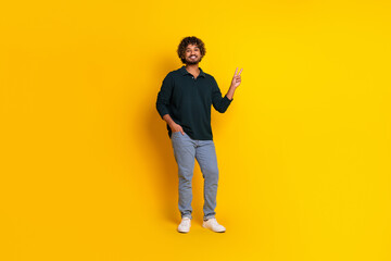 Young man posing with a peace sign against vibrant yellow backdrop, wearing casual black shirt and jeans