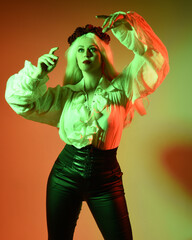 Canvas Print - close up portrait of  blonde female model, wearing vintage gothic fantasy ruffle blouse white shirt, leather pants. gestural pose with hands reaching out casting a spell. colourful studio lighting