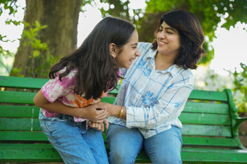 Happy young indian mother and daughter enjoying and having fun together at summer park bench. playful, Childhood, love and bonding.