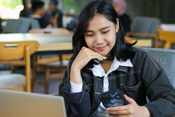 attractive and charming asian woman sitting in cafe using smartphone to browsing cyberspace and read news with laptop on desk, candid