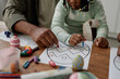 © Seventyfour - Child and adult engaging in Easter egg drawing activity using crayons and paper on wooden table. Hands of both participants carefully working on intricate designs