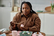 © Seventyfour - African American woman painting easter eggs in bright kitchen preparing for holiday celebrations creating festive atmosphere crafting artistic designs on eggs using brushes and colors
