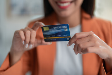 Smiling businesswoman holds a credit card, showing success in online finance. The blurred background hints at a fast-paced global economy