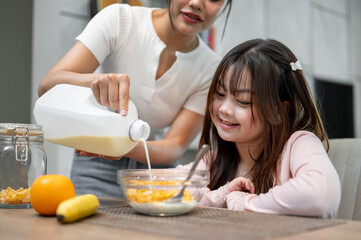 A caring mom is pouring milk from a gallon for her daughter, having cereal as a breakfast.