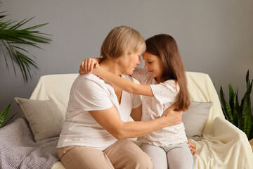 Mature woman hugging her granddaughter sharing gentle cuddle filled with happiness and love elderly grandmother enjoying special family bonding moment with little girl sitting on cozy couch at home