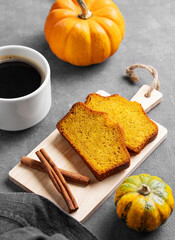 Wall Mural - Slices of pumpkin sweet bread with cinnamon on a wooden board on a dark background with decorative pumpkins and a cup of  coffee.