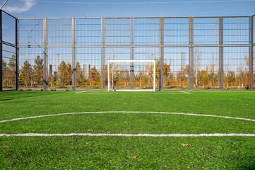 A soccer field featuring a goal and surrounding fences, set in an autumn landscape