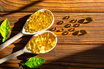 Wooden Spoons Filled with Yellow Capsules. Two wooden spoons are filled with bright yellow capsules, artfully arranged on a wooden surface.