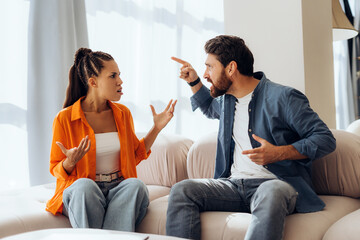 portrait of angry unhappy couple quarreling sitting on sofa at home, gesturing. relationship concept