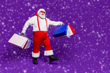 Full length body size view of his he nice cheery glad cheerful positive bearded thick fat Santa carrying bags new clothes clothing going isolated on bright vivid shine vibrant violet lilac background