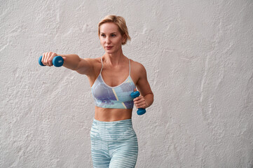 Beautiful young woman in sportswear exercising with dumbbells at the gym. Portrait of a woman trainer in sportswear with dumbbells in her hands one hand out in front straight.