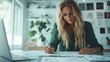 © Maximages  - A blonde woman writes notes in a bright and stylish office, with a laptop open on the table and plant decorations around, conveying diligence and innovation.