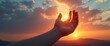© natakot - A silhouette of a hand reaching towards the sky as the sun sets, symbolizing hope and aspiration in a peaceful moment.