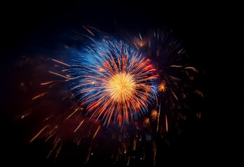 Canvas Print - A single burst of fireworks explodes in the night sky, isolated against a black background.  The fireworks are a mix of red, orange, and blue, creating a dazzling display.