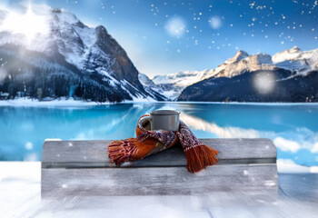 Poster - A warm mug wrapped in a scarf sits on a snowy bench overlooking a frozen lake and snow-capped mountains.